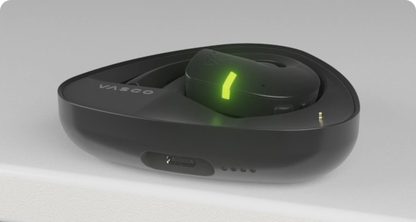 Слушалката Vasco Translator E1 е поставена в зарядния си калъф. Мигащите LED индикатори показват текущото ниво на заряд на калъфа и на слушалката. 